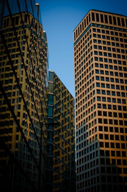 A low-angle view of two tall modern office buildings in Westminster, London, with one building featuring a grid of square windows and the other with a reflective glass facade adorned with a diagonal p